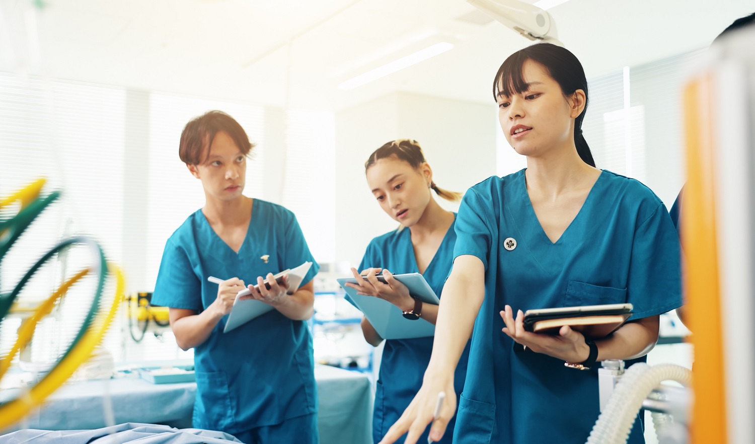 Nursing students with clipboards listen to a colleague in a training lab