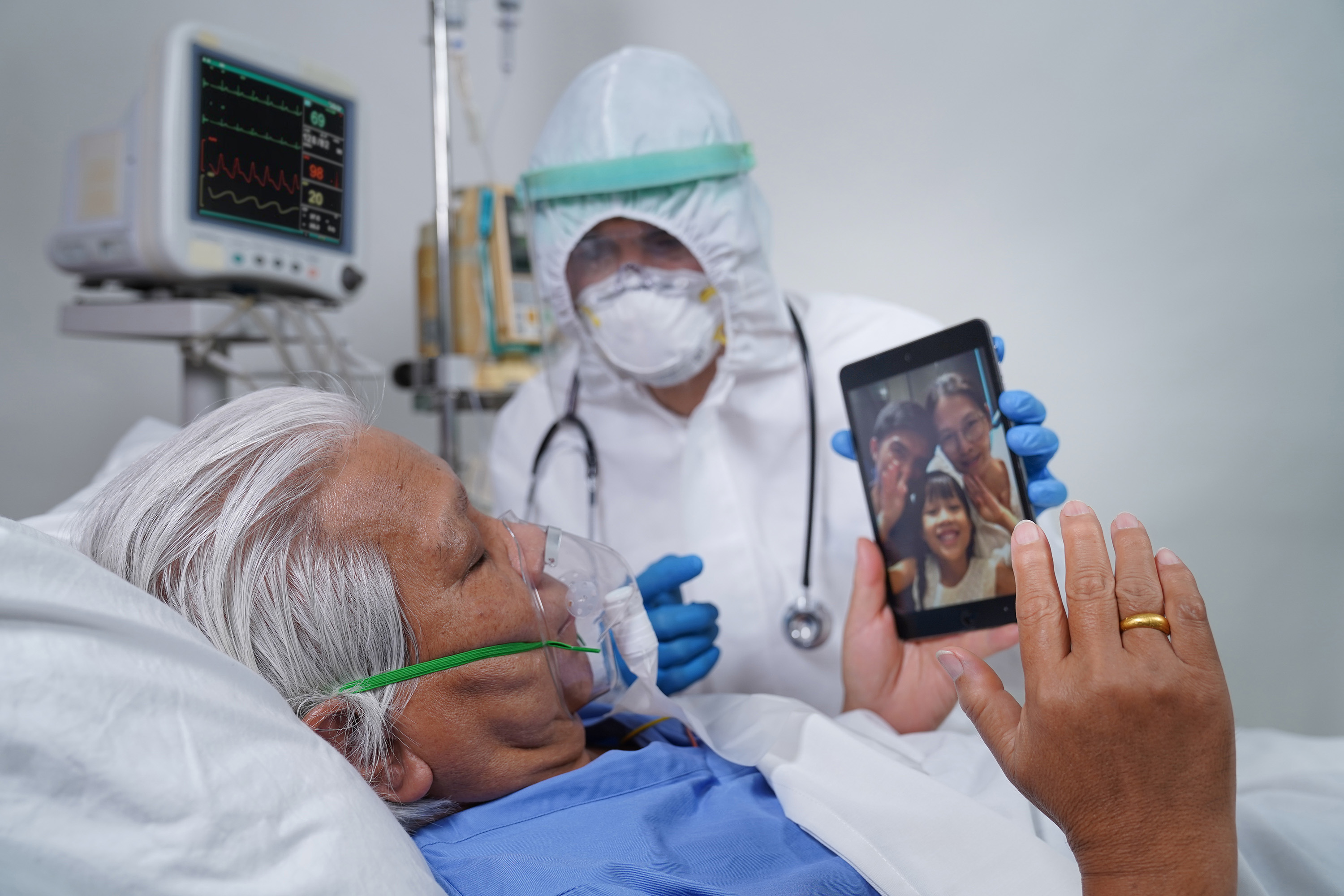 Nurse wearing full PPE helps ventilated patient to speak to their family via video chat